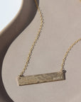 14k gold fill Matriarch Necklace laid on a tan plate in the sunlight. This necklace features either the simple chain and or the April chain and the word "NANA". you can have the option of a smoother or hammered.