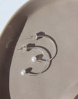 925 sterling silver Balanced Pearl Hoops laid on a tan plate in the sunlight.