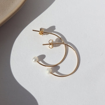 14k gold fill Balanced Pearl Hoops laid on a white plate in the sunlight.