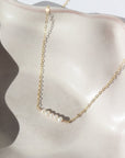 five freshwater pearls lined up on a 14k gold fill simple chain, made by Token Jewelry , photographed on a white ceramic dish