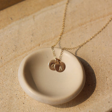 hand stamped letters on a tiny disc hanging from a dainty cable chain. handmade personalized necklace in 14k gold fill