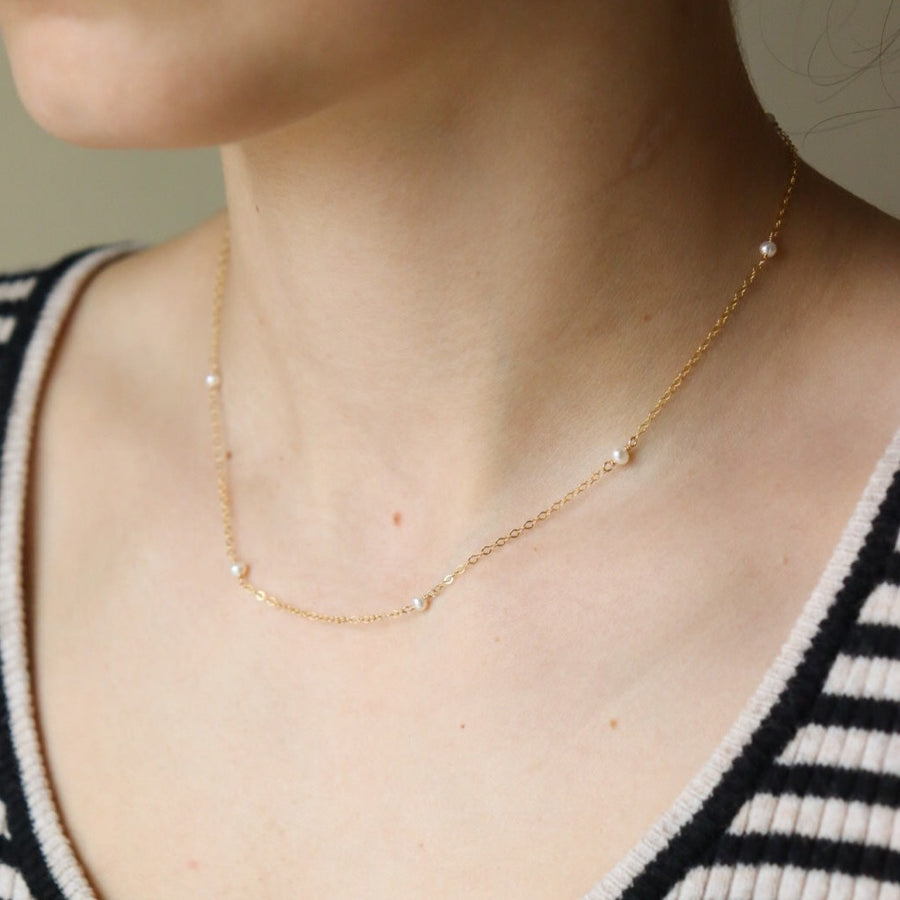 A delicate string of pearl necklace in 14k gold fill photographed on a model at Token Jewelry