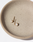 14k gold fill Emma Pearl Studs laid on a gray plate in the sunlight.