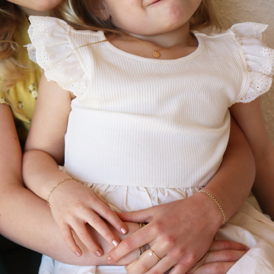 A little girl in a white dress wearing various 14k gold fill Token Jewelry including a bold link chain