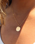 Model wearing 14k gold fill Moon drop necklace in the sunlight. This necklace features our simple chain met by a hammered coin, making it look like the moon.