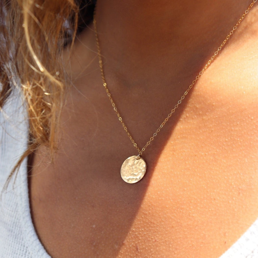 Model wearing 14k gold fill Moon drop necklace in the sunlight. This necklace features our simple chain met by a hammered coin, making it look like the moon.