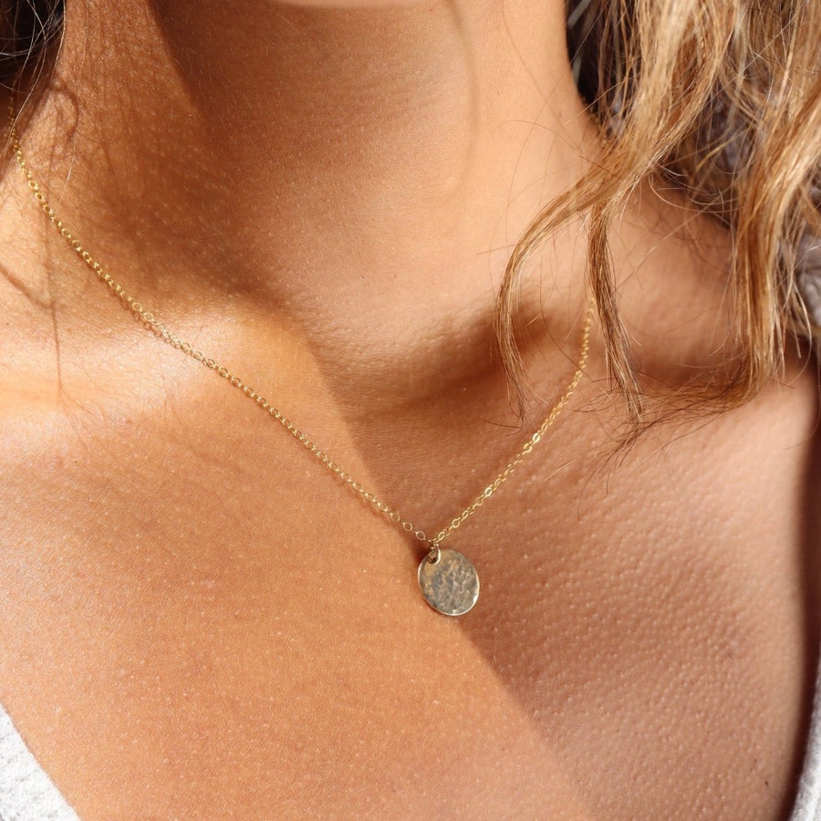 Model wearing 14k gold fill Moon drop necklace in the sunlight. This necklace features our simple chain met by a hammered coin, making it look like the moon.