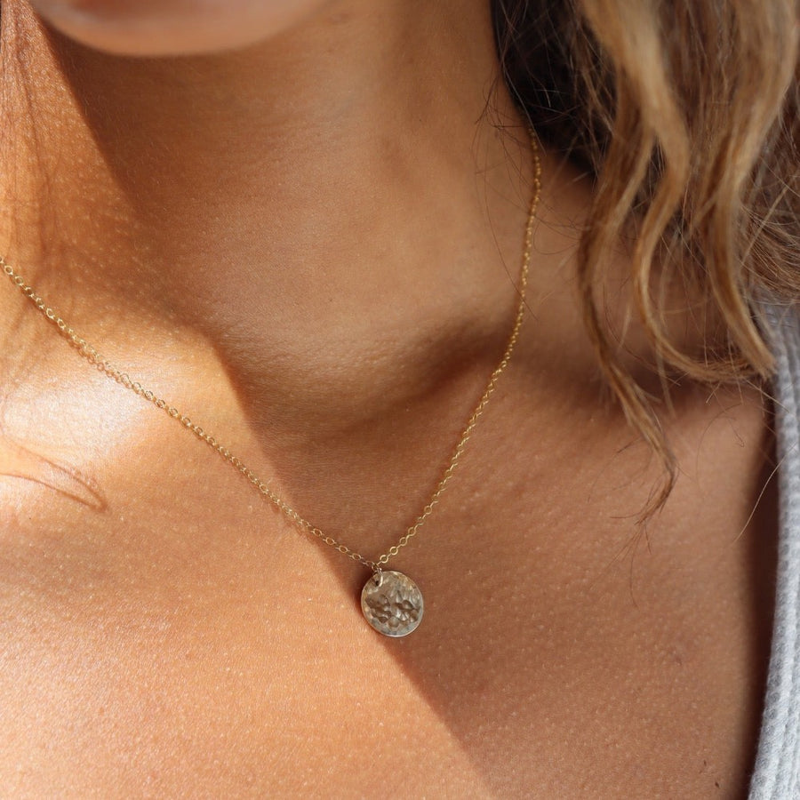 Model wearing 14k gold fill Moon drop necklace in the sunlight. This necklace features our simple chain met by a hammered coin, making it look like the moon.