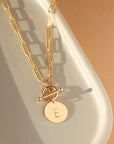 14k gold filled chain link necklace with a toggle clasp and monogrammed "E" flat disk charm, photographed on a white dish