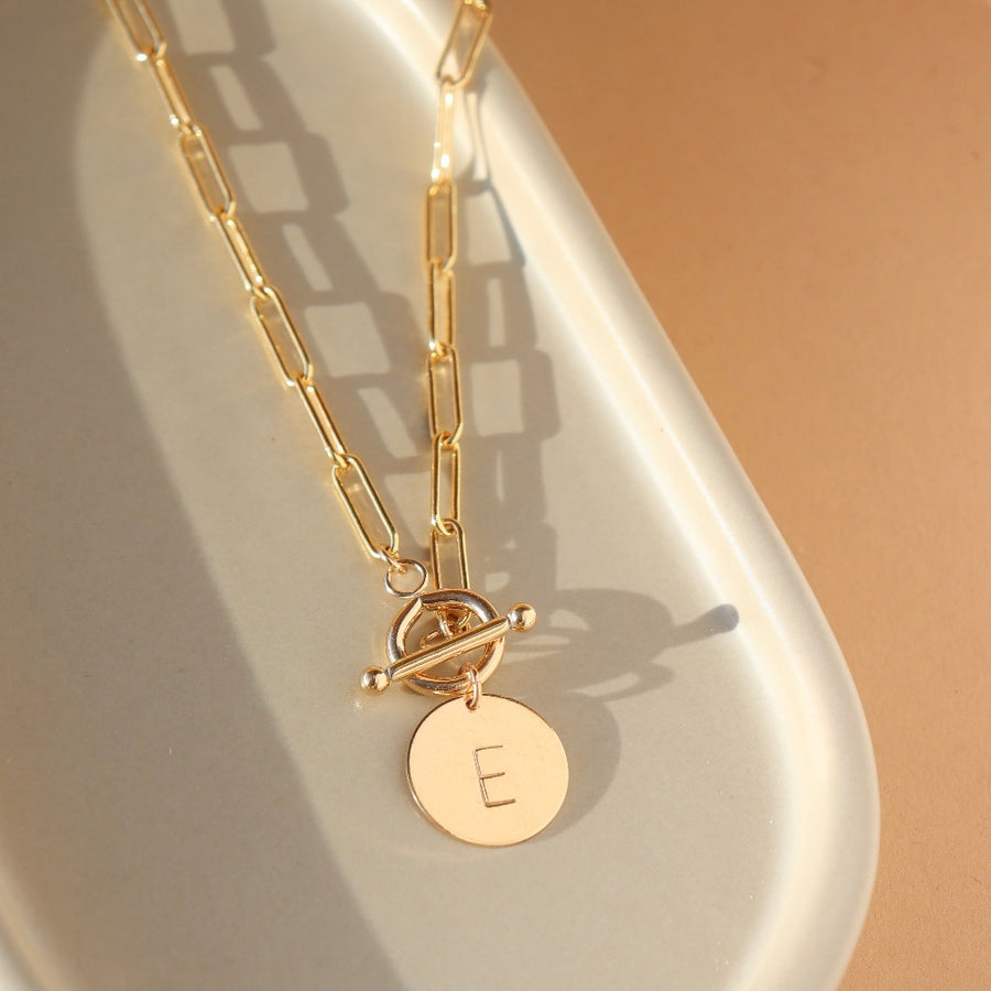 14k gold filled chain link necklace with a toggle clasp and monogrammed "E" flat disk charm, photographed on a white dish