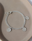 925 sterling silver Carter Personalized disc Bracelet laid on a gray plate in the sunlight. This bracelet features the Carter chain then followed Initial stamped disc.