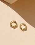 Gold hexagonal stud earrings on a beige background