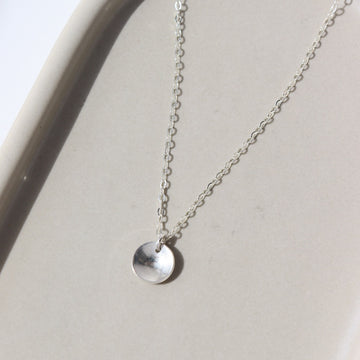 a sterling silver necklace featuring a dainty chain and a small, concave, polished disc