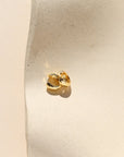 Gold earring on a white cushion against a beige background