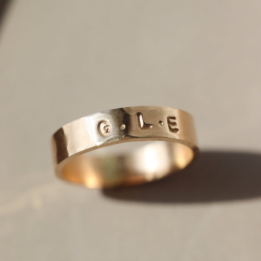 14k gold fill Personalized Cigar Band laid on a tan plate in the sunlight. This ring features the ability to add initials onto your ring.