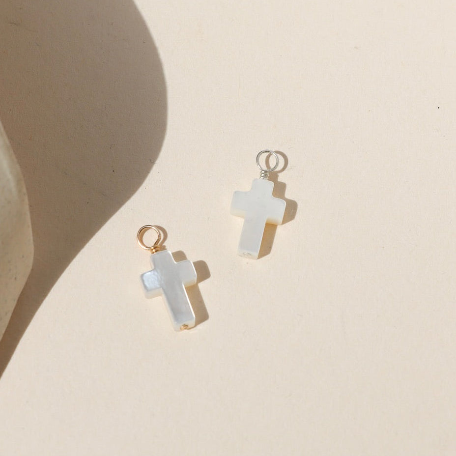 Mother of pearl cross charm with gold or silver hardware on a neutral background.