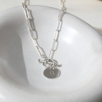 sterling silver chain link necklace with a toggle clasp and monogrammed "B" flat disk charm, photographed on a white dish