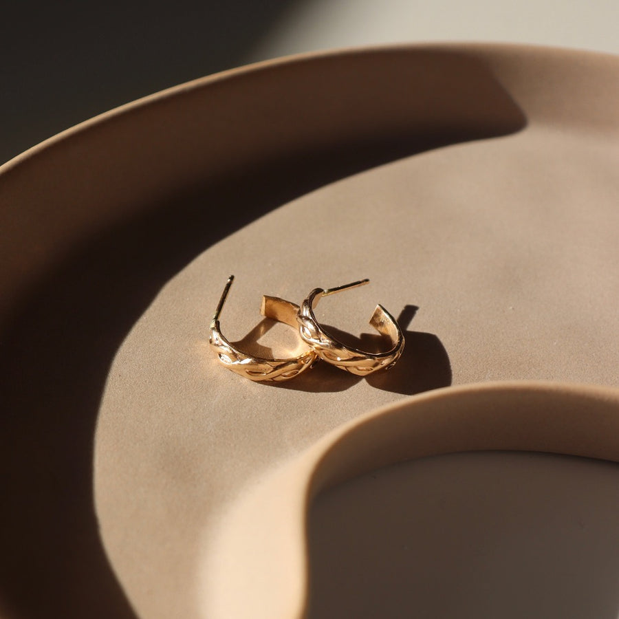 14k gold fill Helix Hoops placed on a brown plate sitting in the sunlight. These earrings feature a small twist like band.