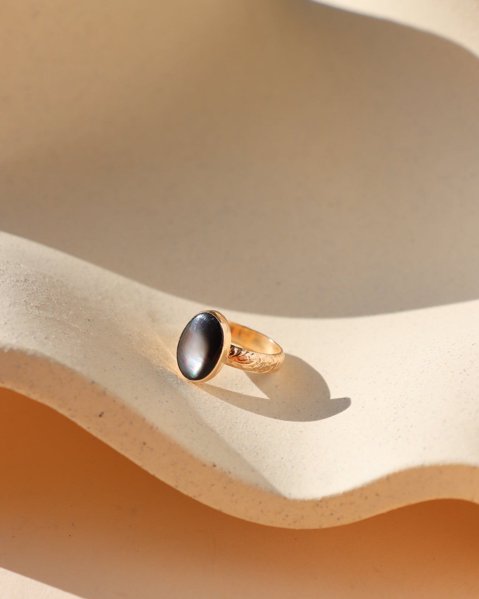Gold fill floral band with a black mother of pearl gemstone on a beige sand-like surface