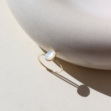 mother of pearl stone set in a bezel on a 14k gold fill skinny ring band, photographed on a table next to a white ceramic dish in the sun