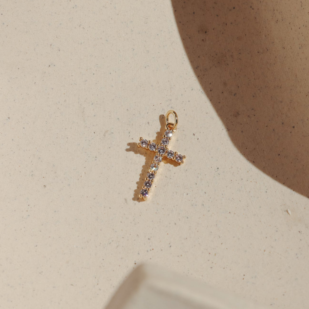 Gold cross charm set with sparkling pavé stones on a neutral background.