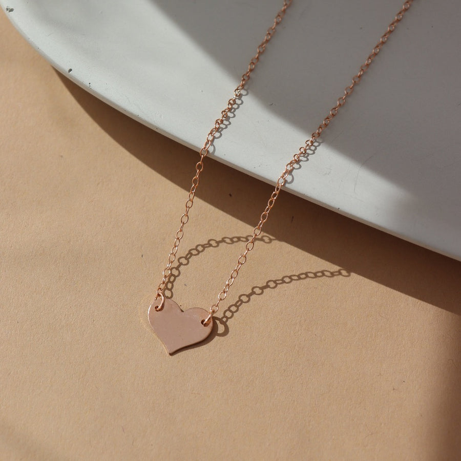 14k Rose gold fill heart necklace on a 14k gold fill chain, photographed on a ceramic dish