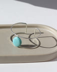 sterling silver double wire cuff bracelet featuring a large turquoise stone wired to the middle. Photographed on a taupe dish in the sunlight