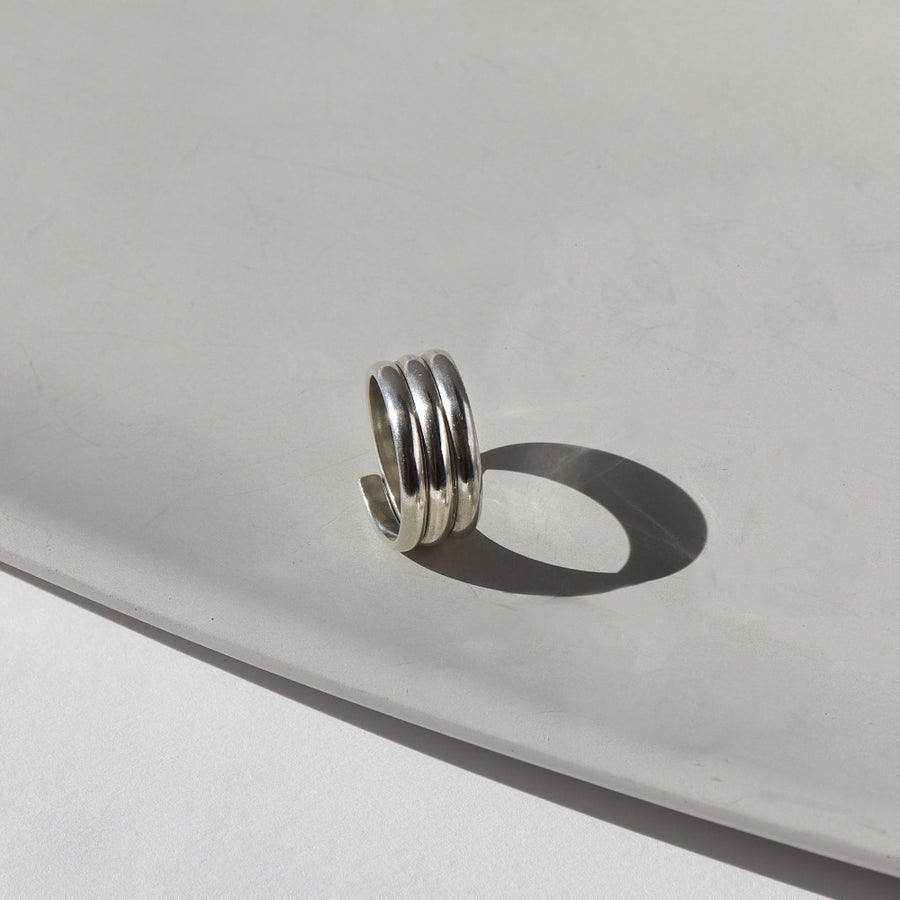 925 Sterling Silver Trinity ring spirals into three bands, photographed on a white sunlit ceramic dish. This ring features the look of the three layered band look but its only one ring.