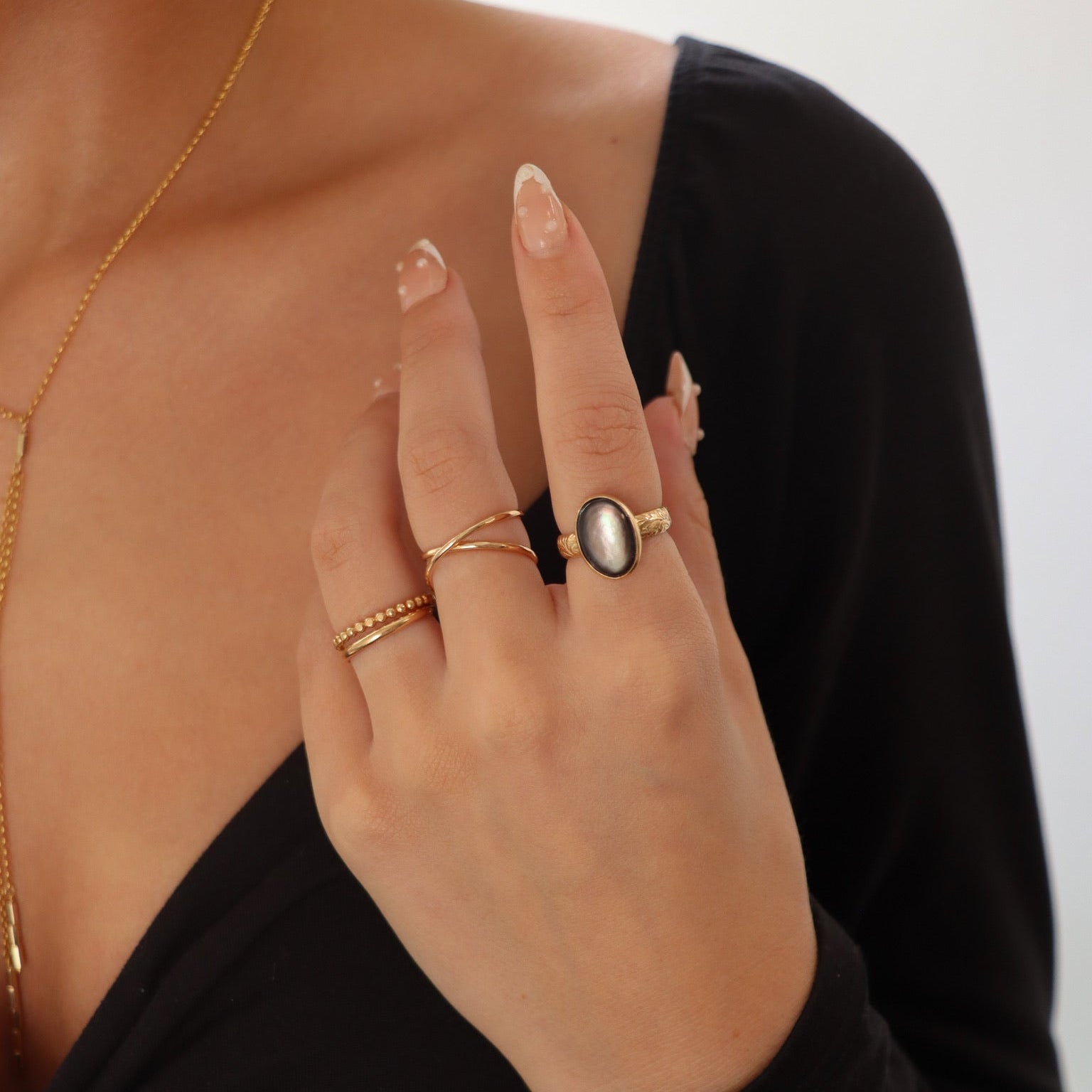 Close-up of gold-filled stacking rings and large black mother of pearl ring with a floral band on a plain background