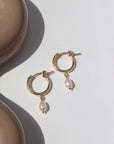 14k gold fill classic pearl hoops laid on a white plate in the sunlight.