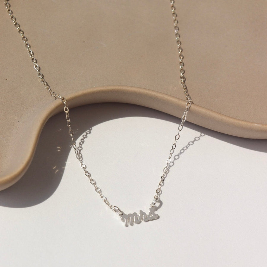 925 sterling silver Mrs.Necklace laid on a white jewelry dish in the sunlight. This is perfect to gift any bride to be in your life.