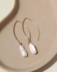 14k Gold fill Juno Earrings laid on a tan plate in the sunlight. Perfect for your wedding fits.