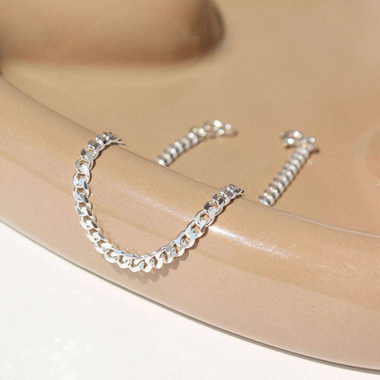 925 sterling silver cuban style chain link bracelet, laid out on a curvy ceramic dish  Edit alt text