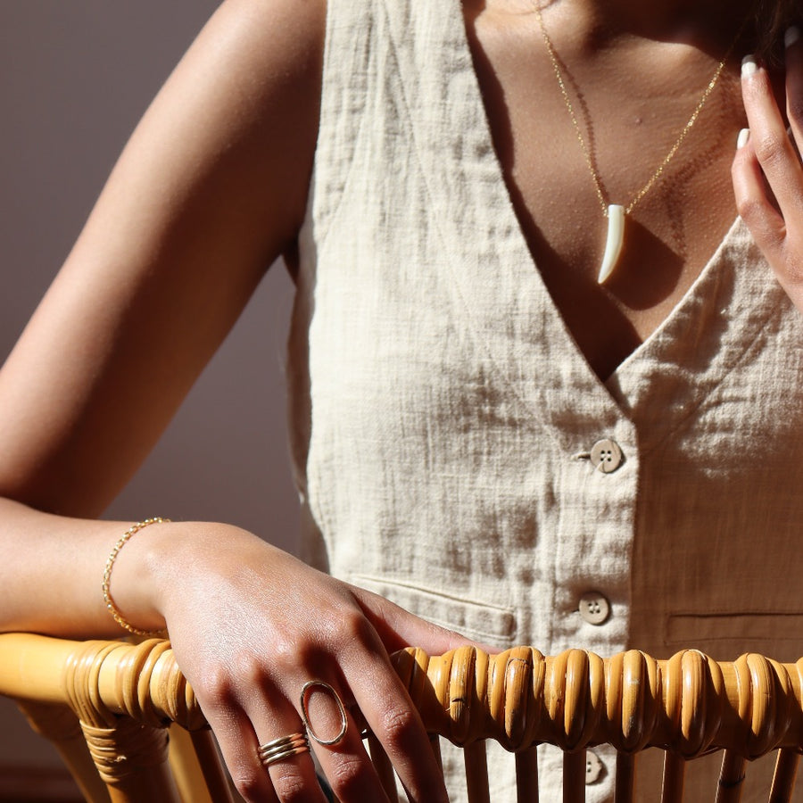 a tusk-shaped pendant made of mother of pearl on a 14k gold fill chain, photographed on a brunette model in the sunlight wearing other 14k gold fill jewelry made by Token Jewelry