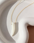 a tusk-shaped pendant made of mother of pearl on a 14k gold fill chain, photographed on a white ceramic dish