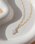 a mother of pearl white cross pendant on a 14k gold fill chain, lying on a white ceramic dish