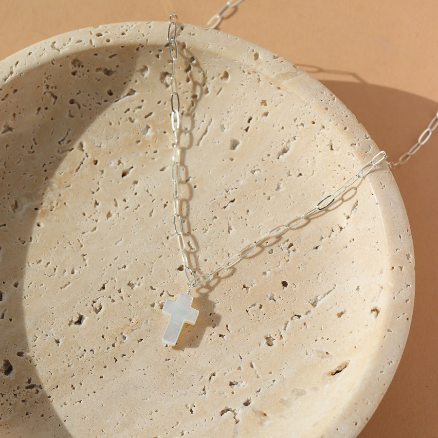 a mother of pearl white cross pendant on a 925 sterling silver chain, lying on a white ceramic dish