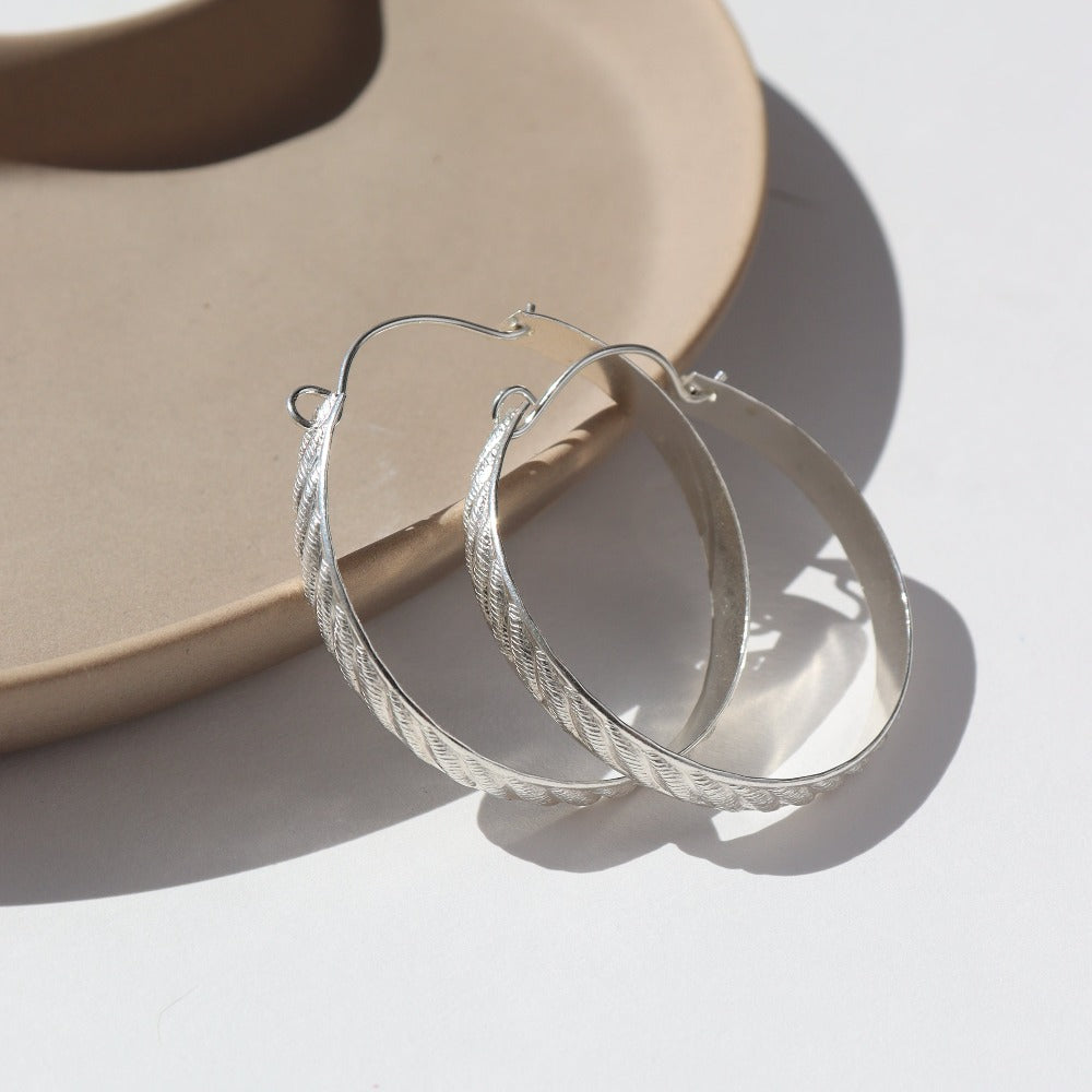 Sterling silver ripple hoops resting on a brown ceramic dish