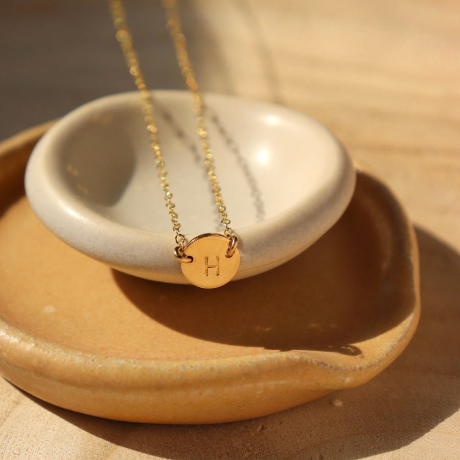 white and tan colored plate with a 14k gold fill necklace laid across featuring a circle pendent with initial anchored in the middle with the simple chain. Anchored Monogram Necklace - Token Jewelry