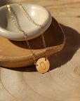 white and tan colored plate with a 14k gold fill necklace laid across featuring a circle pendent with initial anchored in the middle with the simple chain. Anchored Monogram Necklace - Token Jewelry