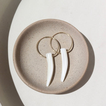 14k gold fill tusk hoops laid on a tan plate in the sunlight.
