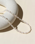 14k gold fill Endless pearl Necklace laid on a white paper in the sunlight.