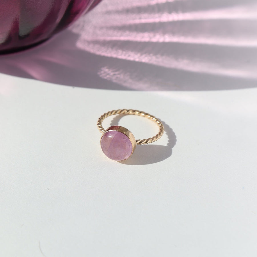 925 Sterling Silver Pippa Ring laid on a white paper in the sunlight. This ring features a sprial band with a pink kunzite gemstone.