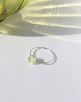 925 Sterling silver Sweet Pea Ring laid on a white plate. This ring features a simple smooth band with a round Prehnite gemstone.