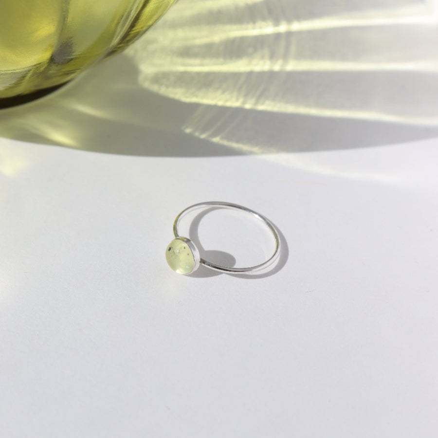 925 Sterling silver Sweet Pea Ring laid on a white plate. This ring features a simple smooth band with a round Prehnite gemstone.