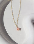 14k gold fill Cherry Blossom Necklace placed on a white jewelry plate in the sunlight. This Necklace features a simple chain with a dangle gemstone. The gemstone that is featured in this necklace is the Cherry Agate Sphere.