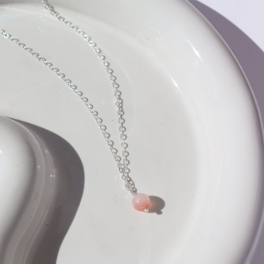 925 Sterling Silver Necklace laid on a white jewelry plate in the sunlight.  This Necklace features a simple chain with a dangle gemstone. The gemstone that is featured in this necklace is the Cherry Agate Sphere.