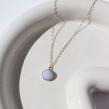 14k gold fill Blue Lace Agate Necklace laid on a white plate in the sunlight. This Necklace features our simple chain along with a Blue Lace Agate gemstone.