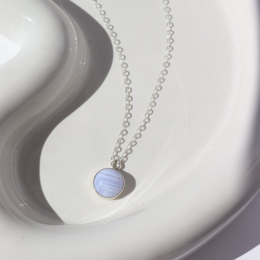925 sterling silver Blue Lace Agate Necklace placed on a white plate in the sunlight. This Necklace features our simple chain along with a Blue Lace Agate gemstone.