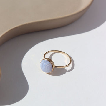 14k gold fill Blue Lace Agate Ring laid white paper in the sunlight. This Ring Features a simple band with light hammering around the sides, this ring also features the Blue Lace Agate Ring.